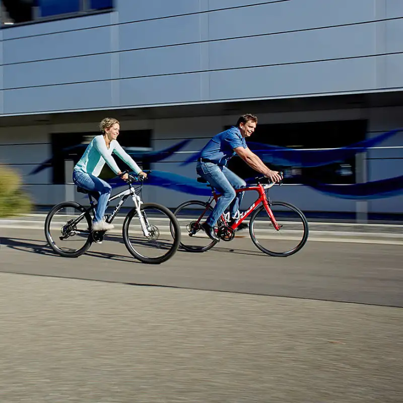 Zwei Menschen, die auf zwei Stadträdern vor einem Büro-Gebäude vorbeifahren