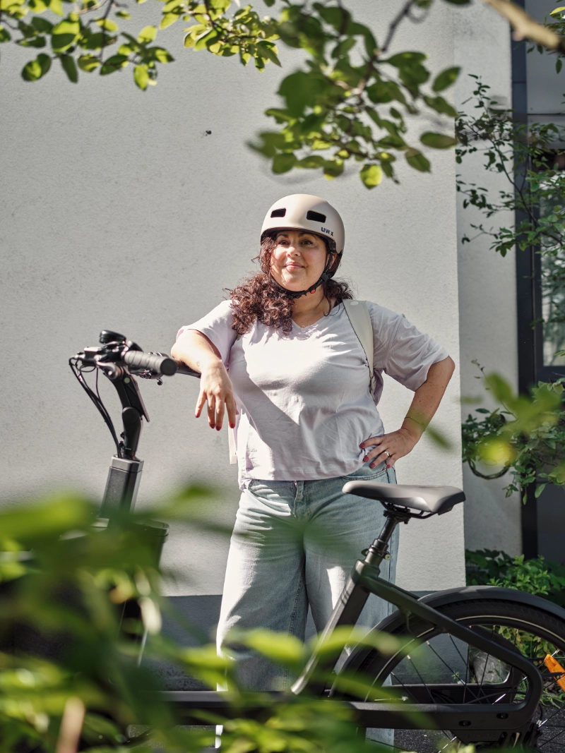 Frau mit Locken lehnt am JobRad, im Vordergrund Pflanzen